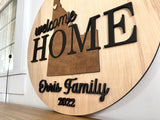 Welcome Home round wood sign with a silhouette of Idaho, featuring the family name and the year. Perfect for hanging in the entryway of a new home