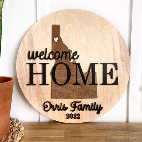 Welcome Home round wood sign with a silhouette of Idaho, featuring the family name and the year. Perfect for hanging in the entryway of a new home