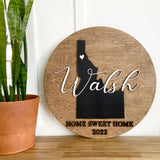 Round wood sign with a silhouette of Idaho and the last name featured through the center, and 'HOME SWEET HOME' written at the bottom