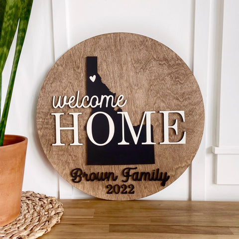 Round wood sign with a silhouette of Idaho and the words welcome HOME going through it.  Family name at the bottom in black lettering.